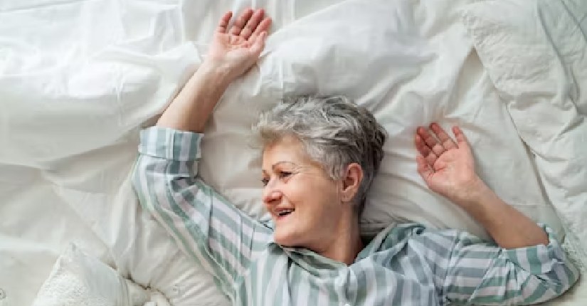 Elderly woman waking up refreshed in bed, smiling and relaxed, showing good sleep benefits for healthy aging