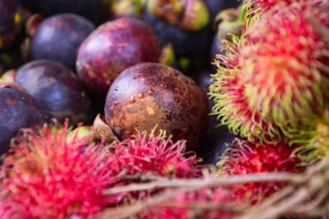 A close-up of a fresh rambutan, one of the lesser-known fruits and vegetables, showcasing its hairy red shell and juicy white flesh inside, placed on a simple background.